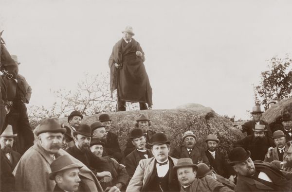 Hermann Allmers auf einem Stein stehend mit Männern im Vordergrund